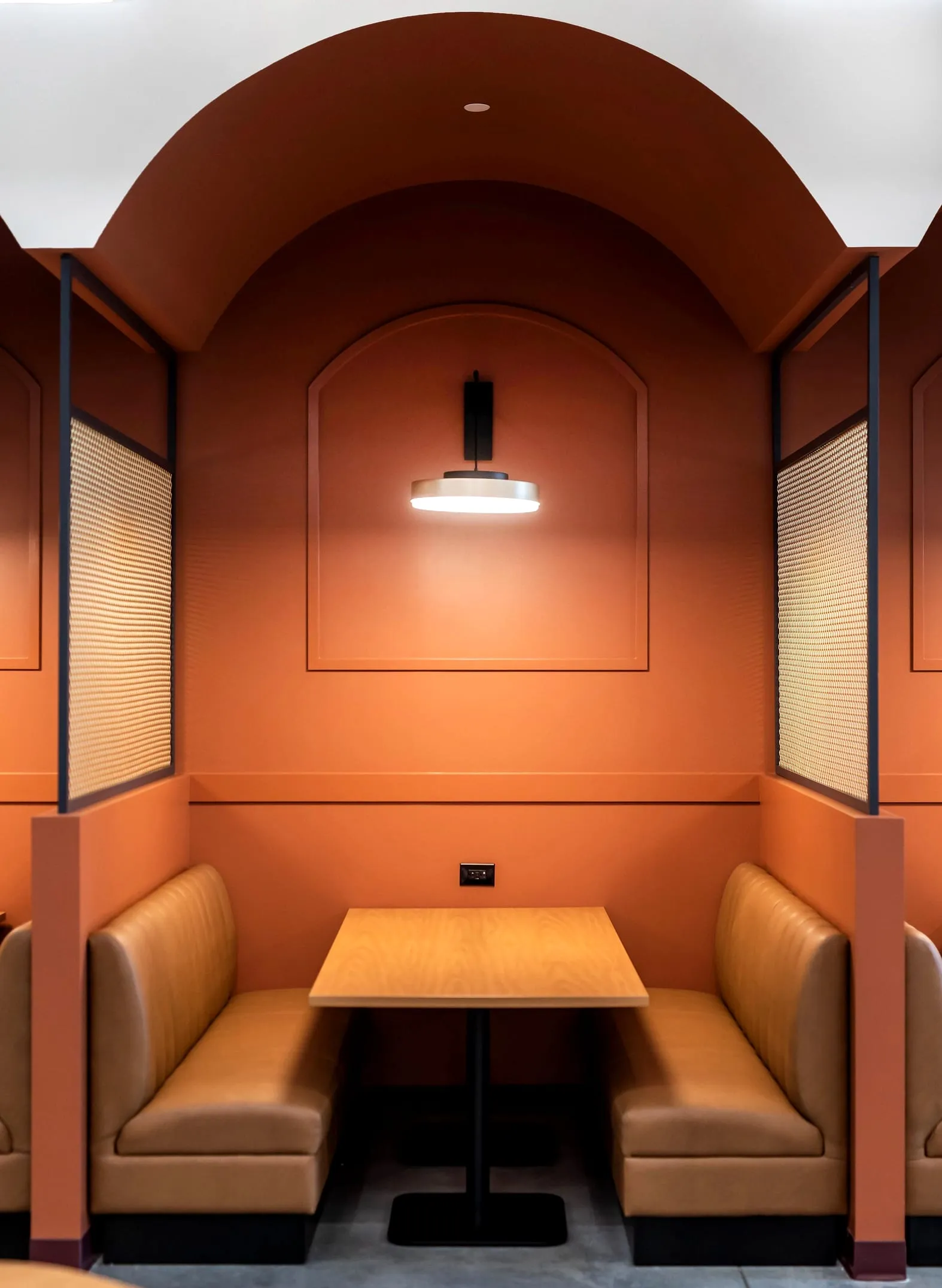 An arched terracotta booth with leather benches either side of a table