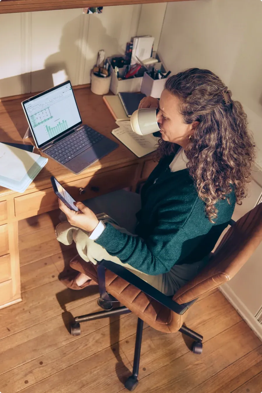 A woman working on a laptop at a wooden desk, seen from above.