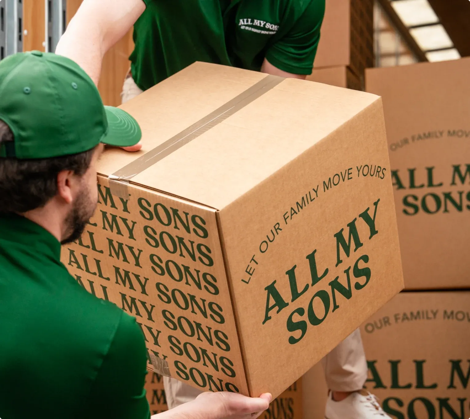 An All My Sons mover in a green cap carrying a branded box.