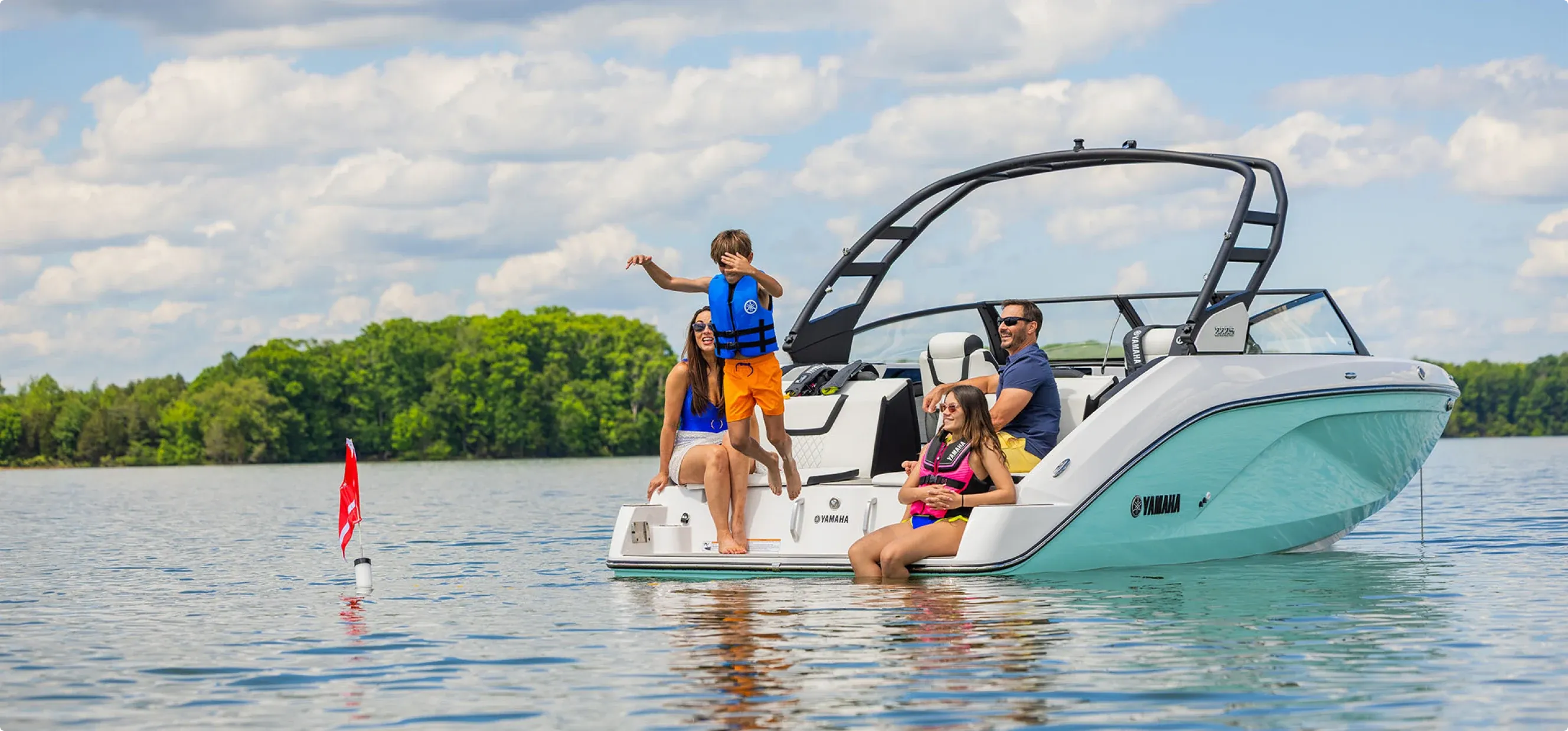 Friends on the bow of a Yamaha sport boat on a sunny lake.