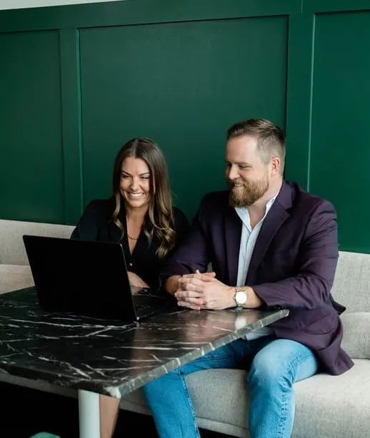 Two colleagues on a sofa in a green booth, smiling over a laptop