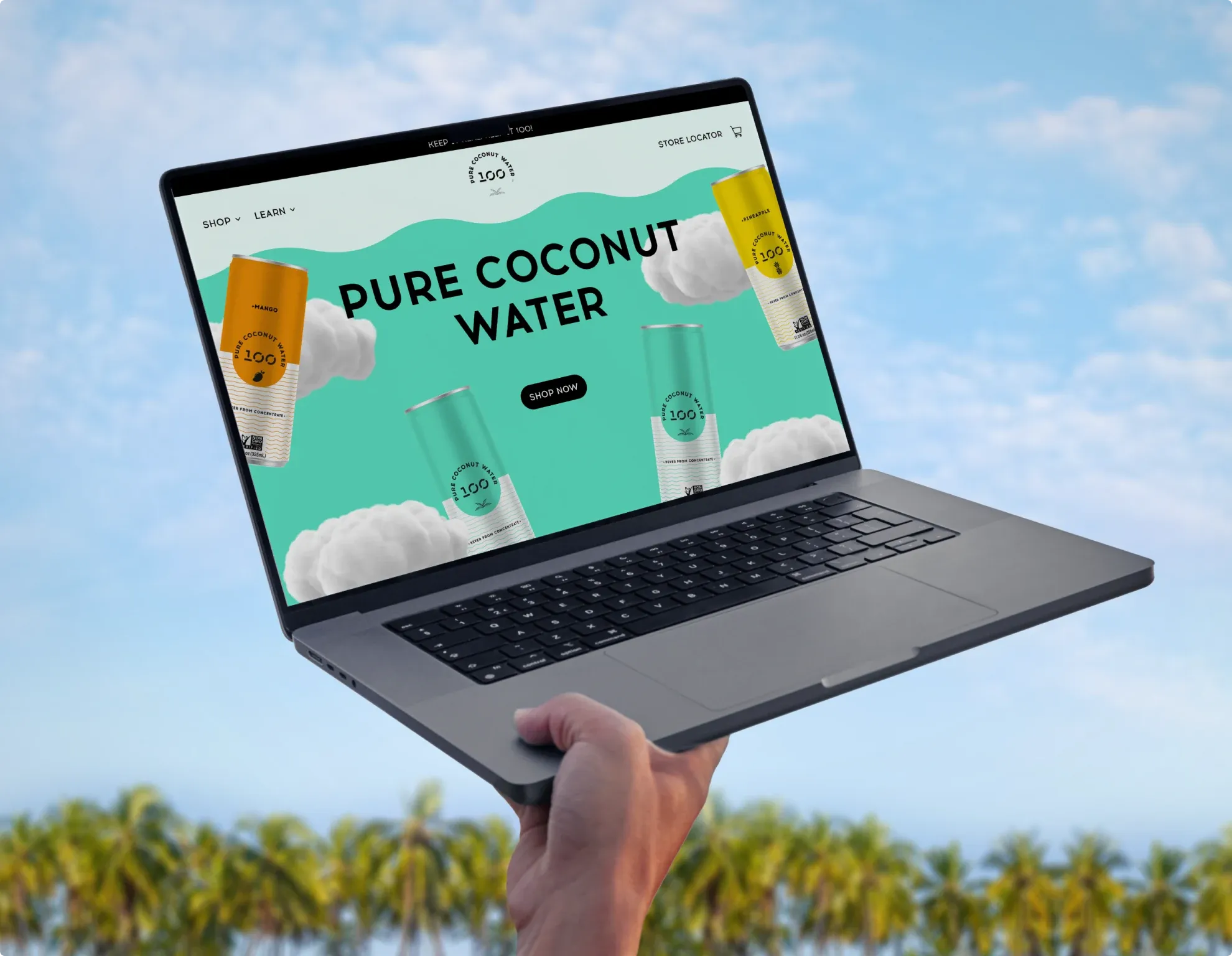 A hand holding up a laptop open on the 100 Coconuts site, “Pure Coconut Water”, against a sky over palm trees.