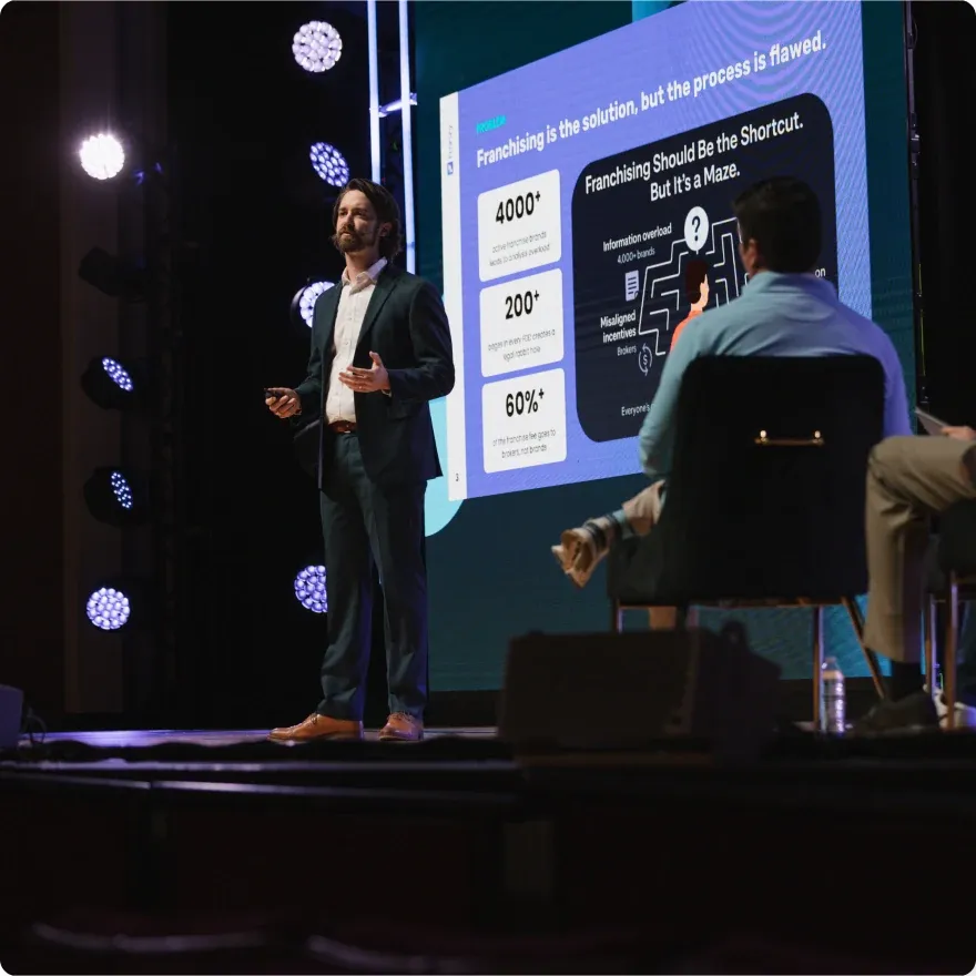 A speaker presents on the Venture Atlanta stage in front of a slide about franchising.