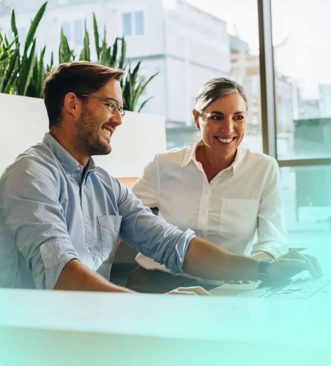 Two Sayers colleagues smiling over a laptop by an office window.
