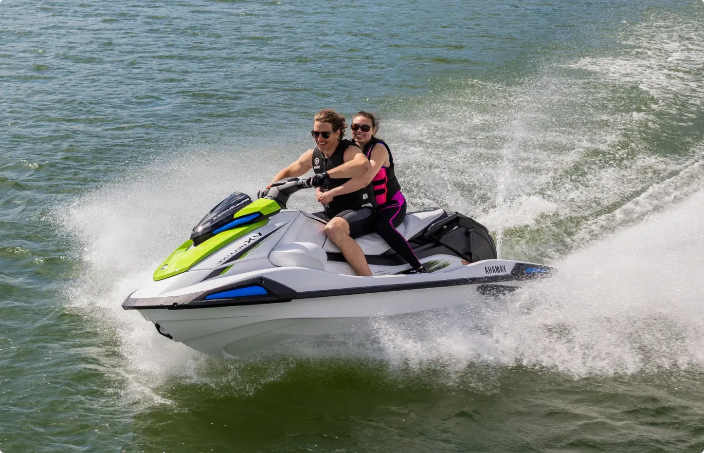Two riders on a Yamaha WaveRunner throwing spray across green water.