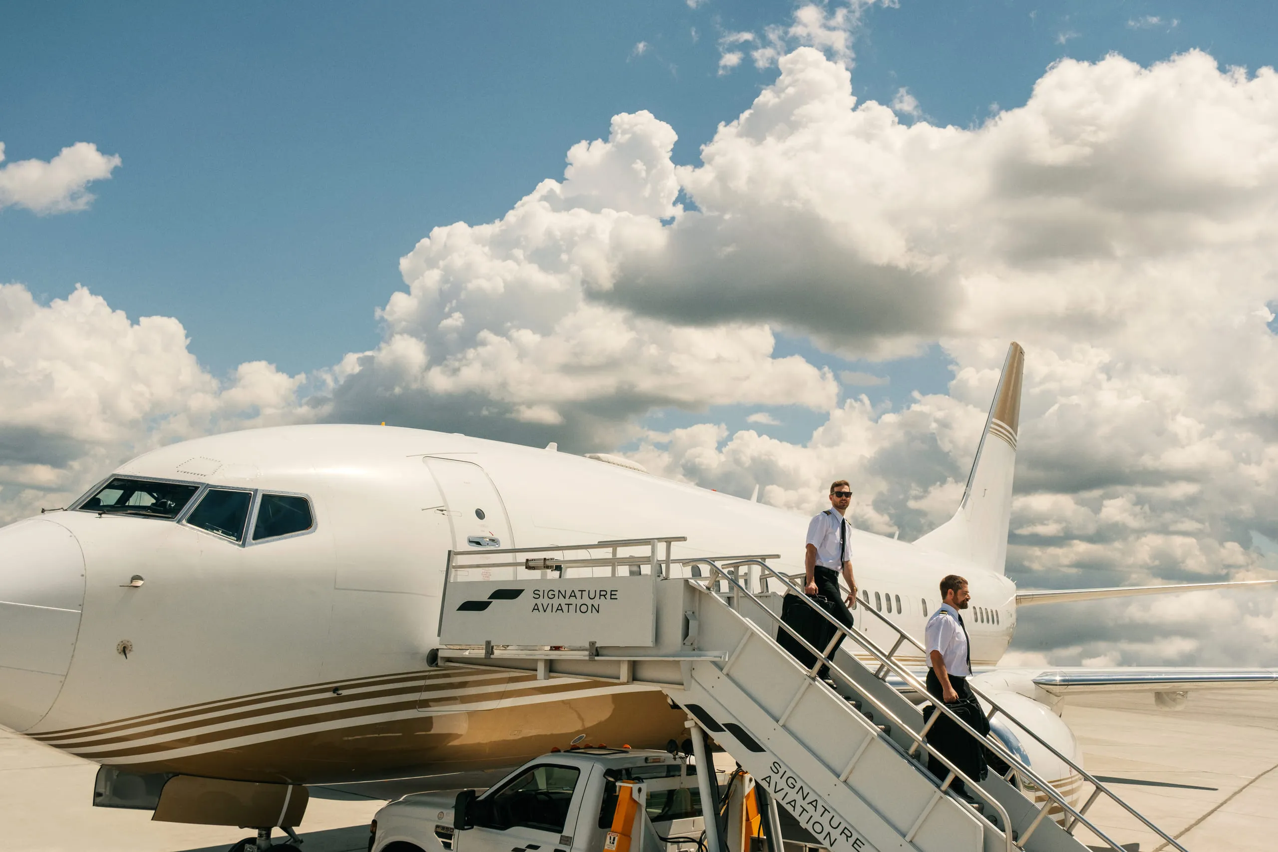 Two pilots walking down the airstair of a Signature Aviation jet under a bank of cumulus cloud.