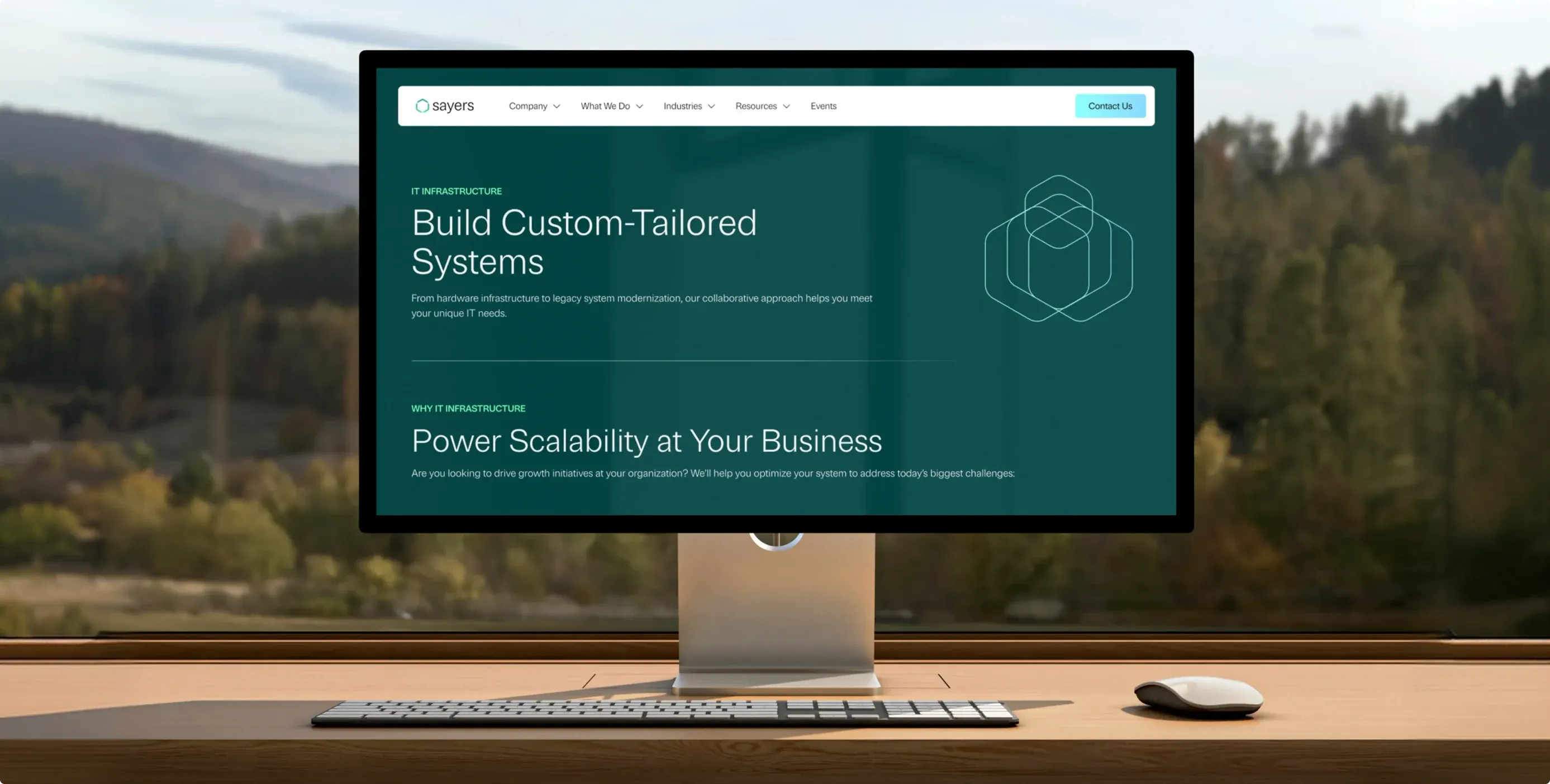 The new Sayers website on a desktop monitor by a window onto pine hills: “Build Custom-Tailored Systems.”