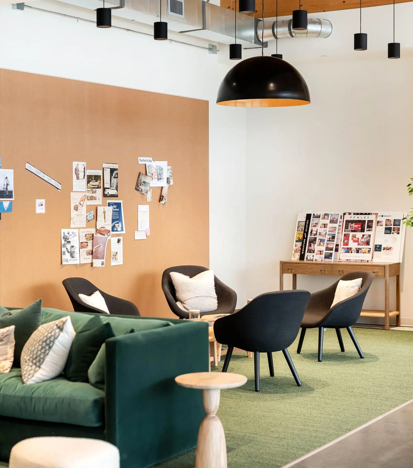 A studio lounge with a green sofa facing a wall of pinned moodboards